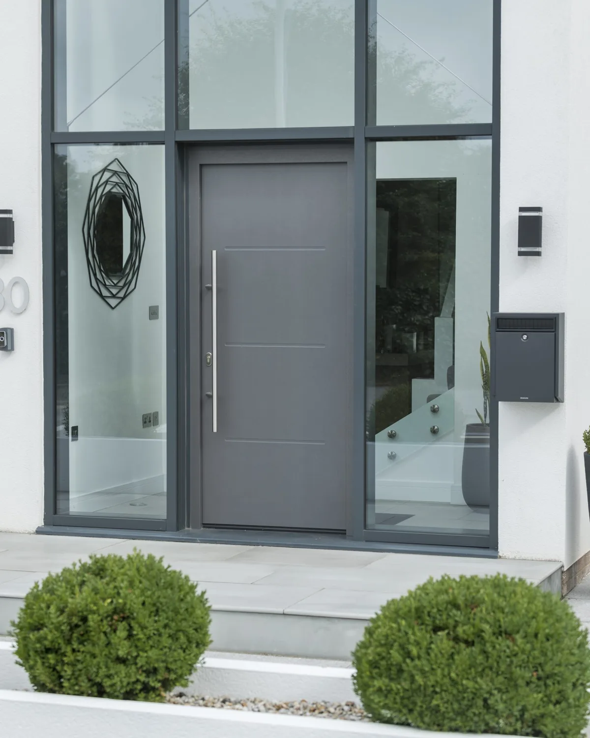 Grey aluminium designer front door with a round glazed panel and full-height pull handle