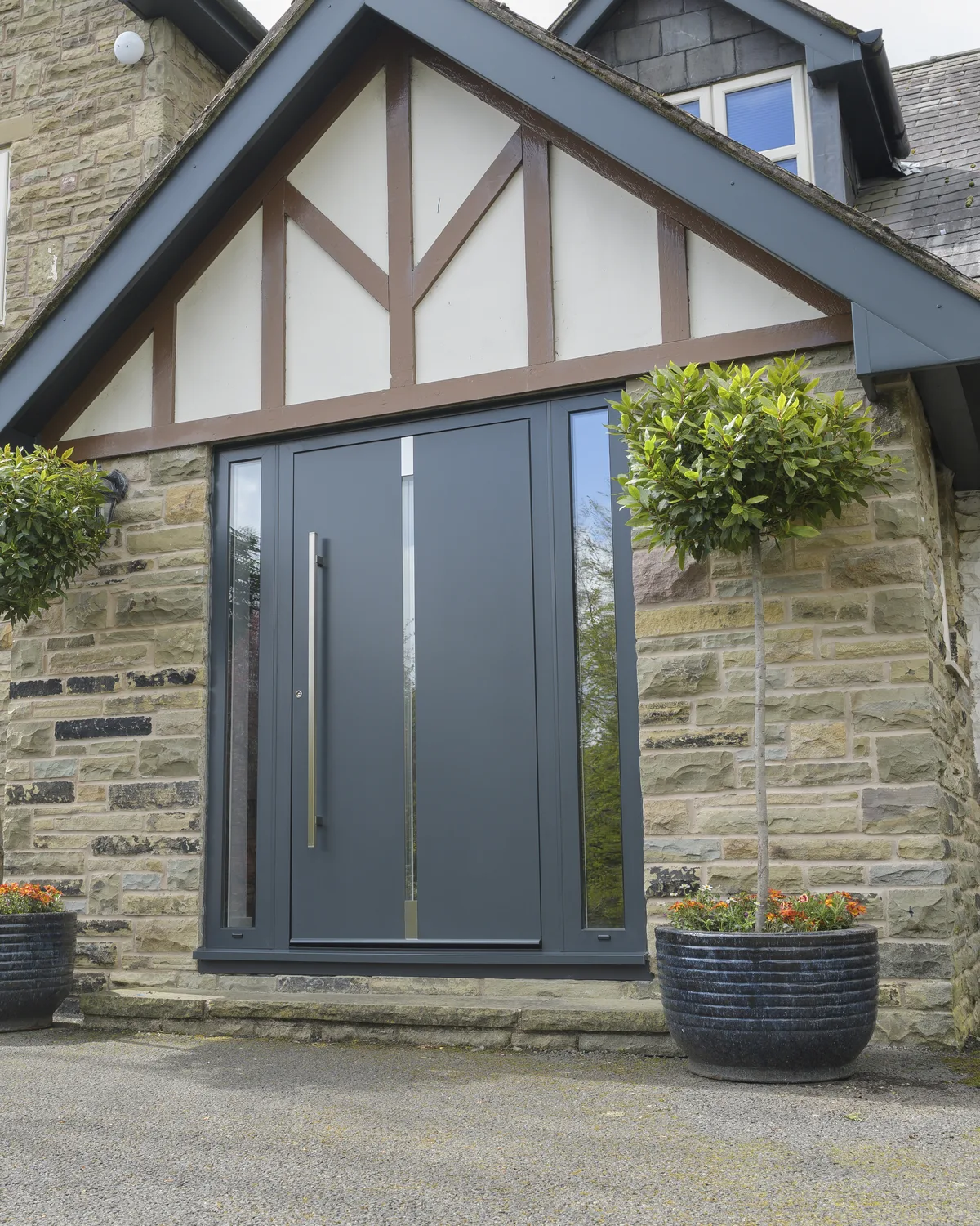 Grey aluminium entrance door with vertical slats on a mock-Tudor house with bay trees