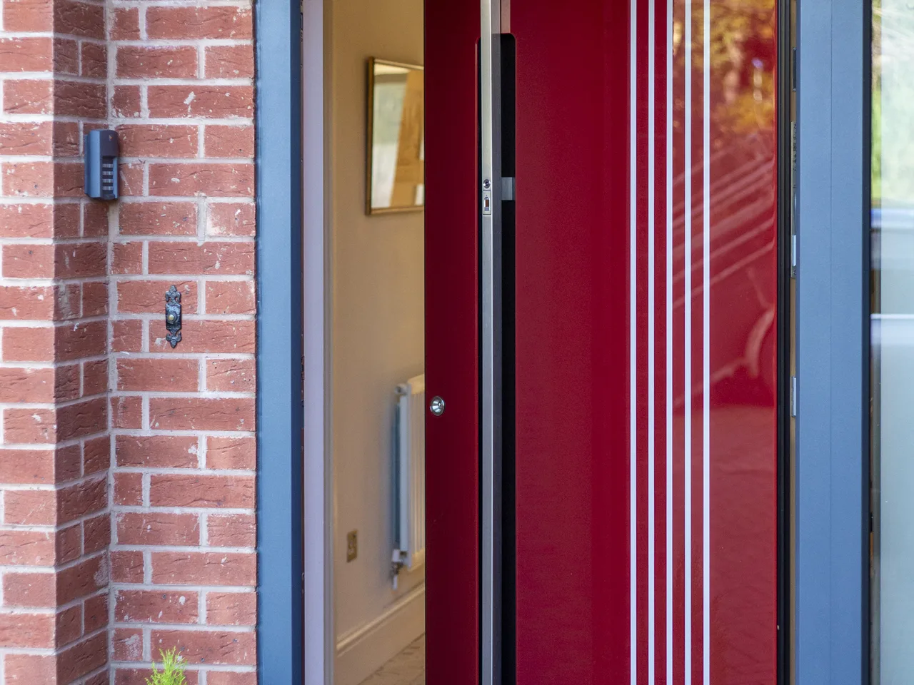 Red aluminium entrance door standing open in a brick porch