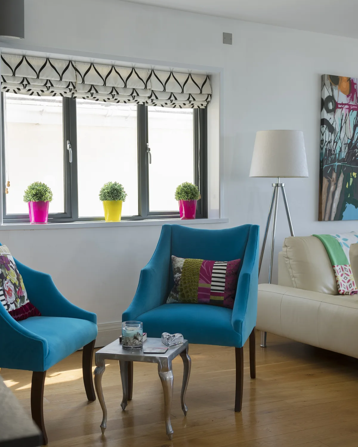 Lounge with grey aluminium windows, teal armchairs and a view of the garden