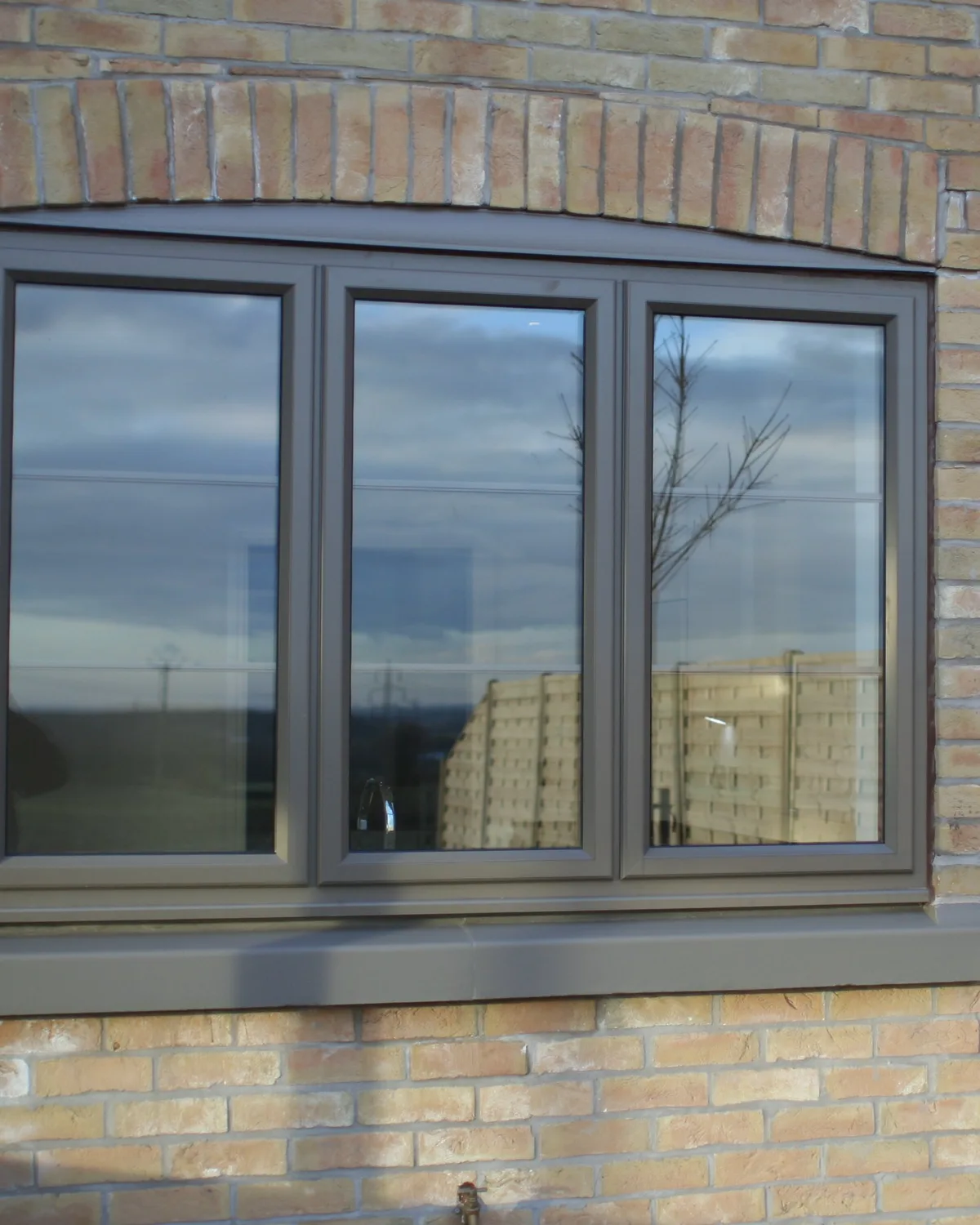 Grey flush aluminium casement window set in a pale brick wall