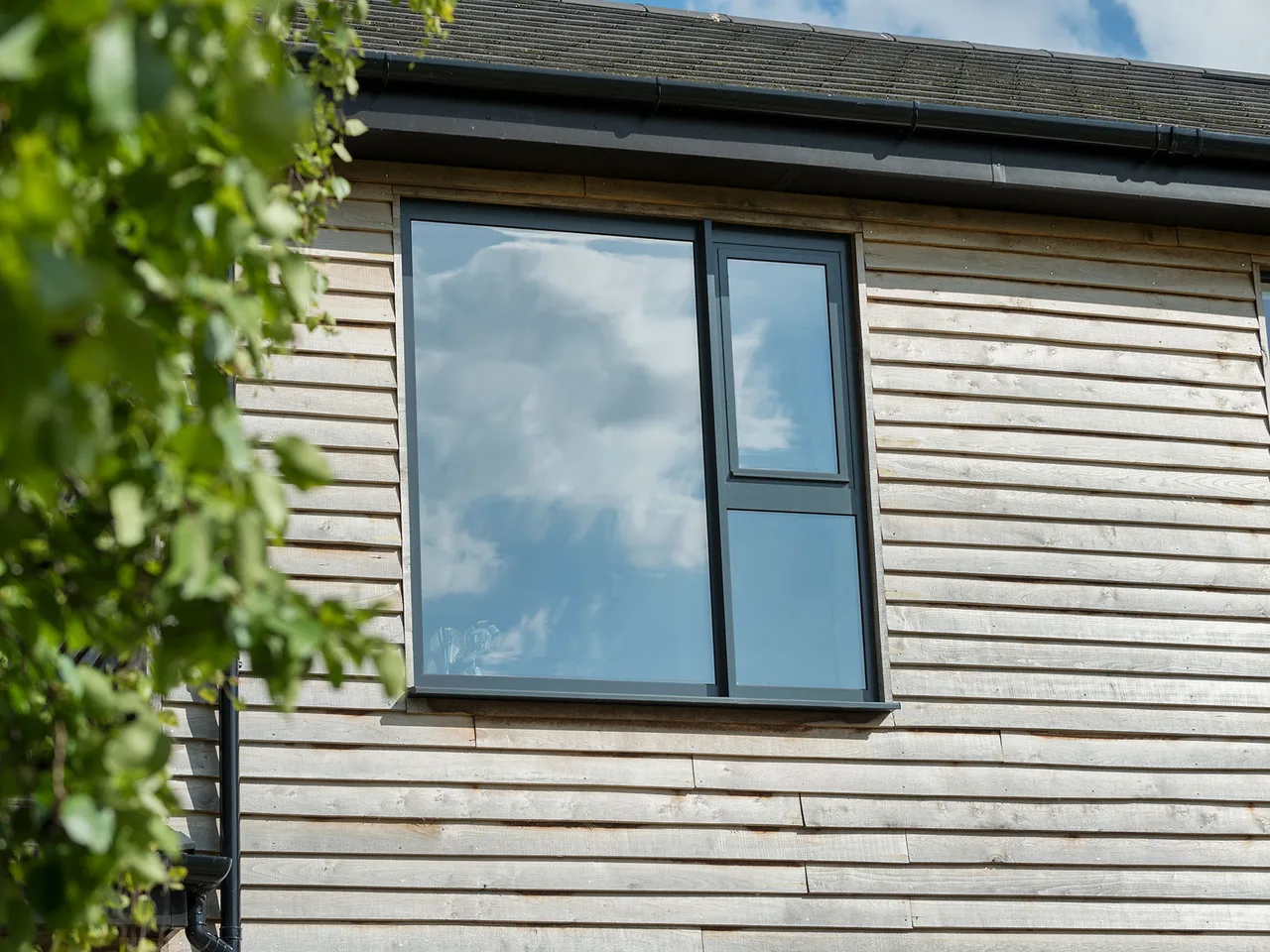 Grey aluminium window set into a timber-clad wall, close view of the frame