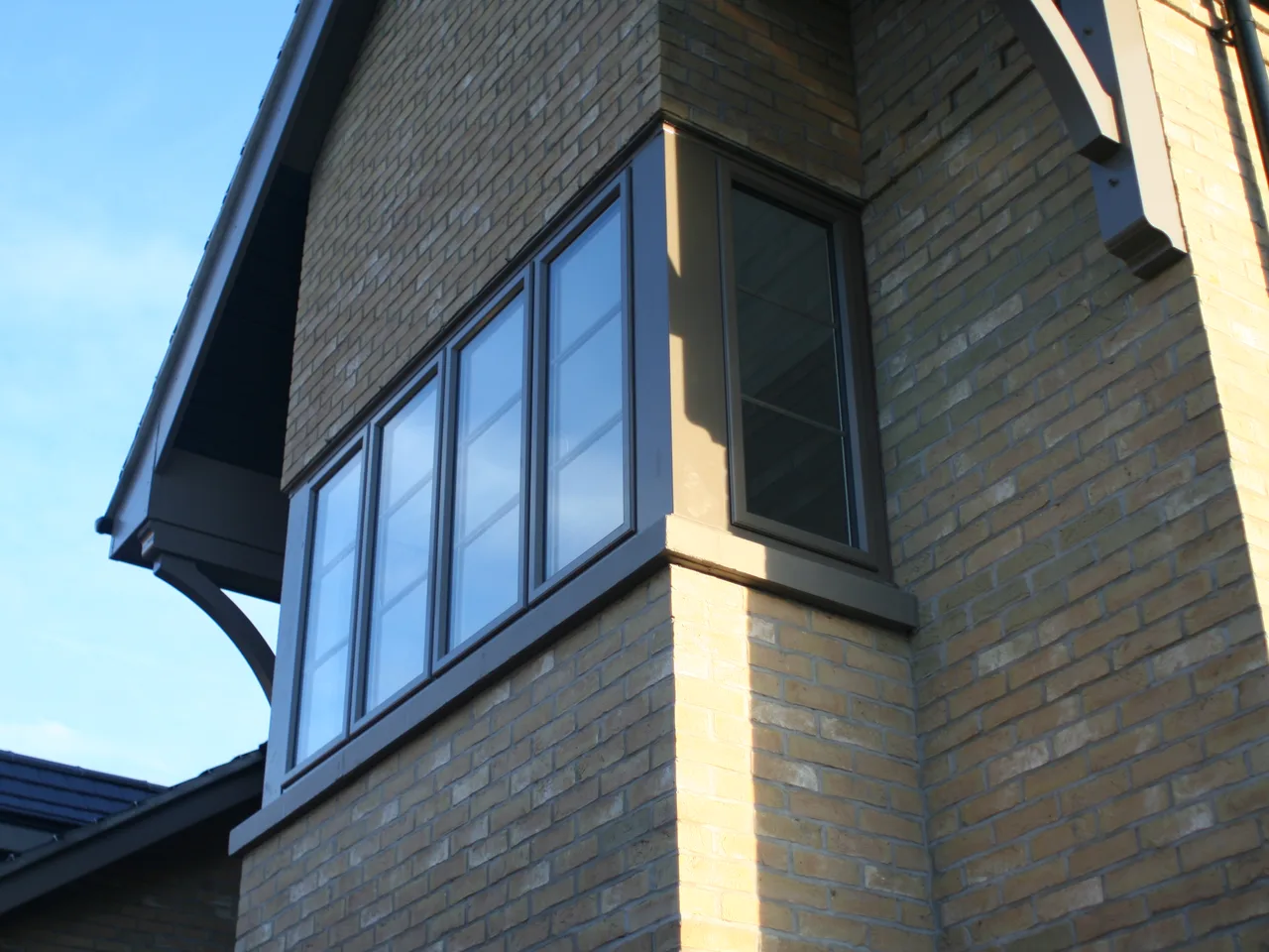 Dark grey aluminium windows on a brick and render house with a bay corner