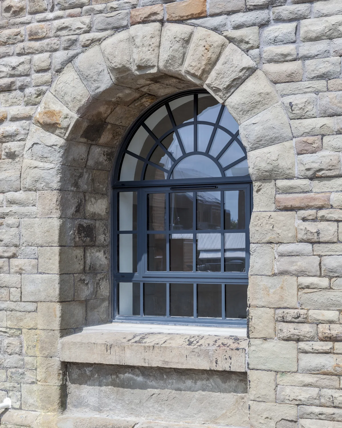 Dark grey aluminium heritage window with sunburst glazing bars set in a round stone arch