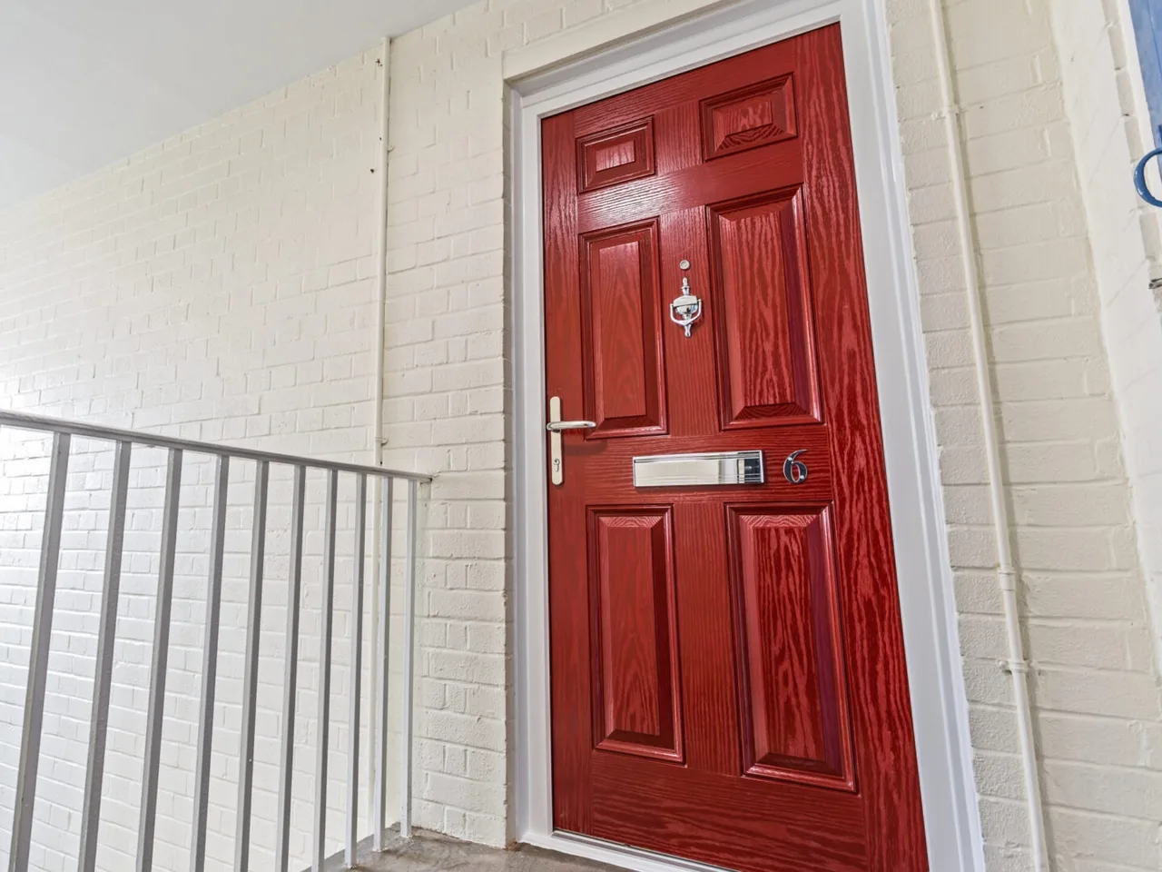 Red flat-entrance fire door with brass letterplate on a white landing with stair railings