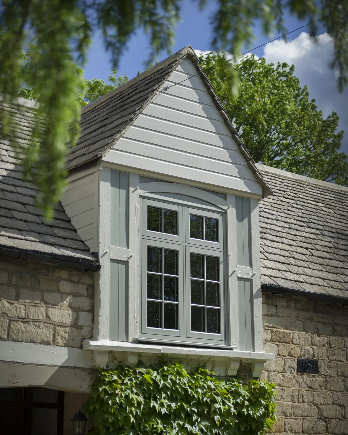 Pale grey flush casement window in a stone-faced dormer on a slate roof