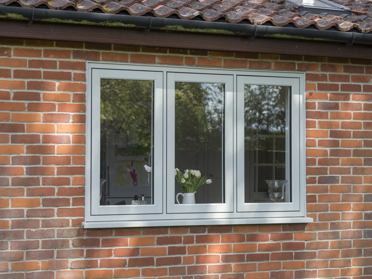 Pale grey flush casement window set in a red brick cottage wall