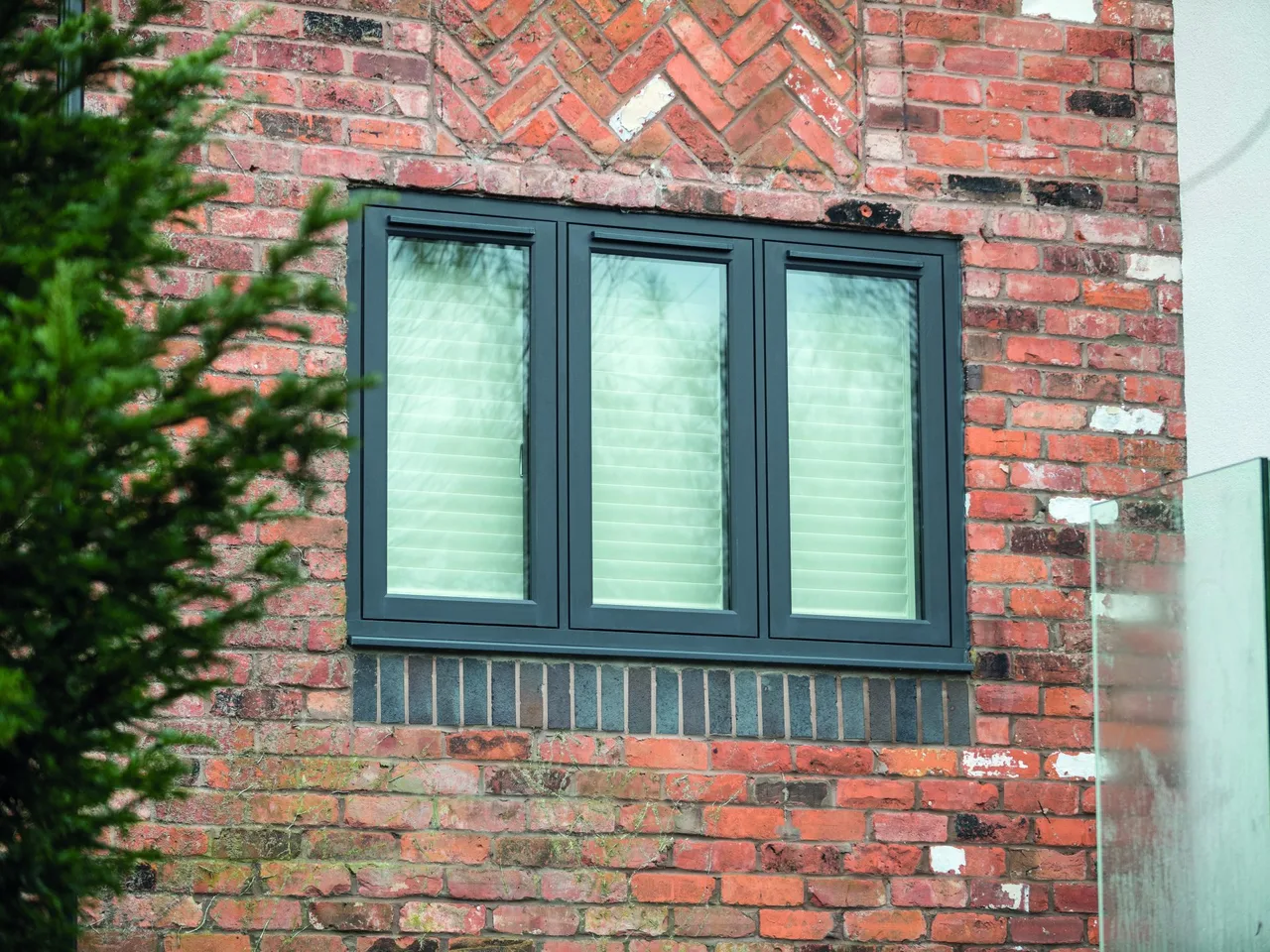 Dark grey flush casement window in an old red brick wall