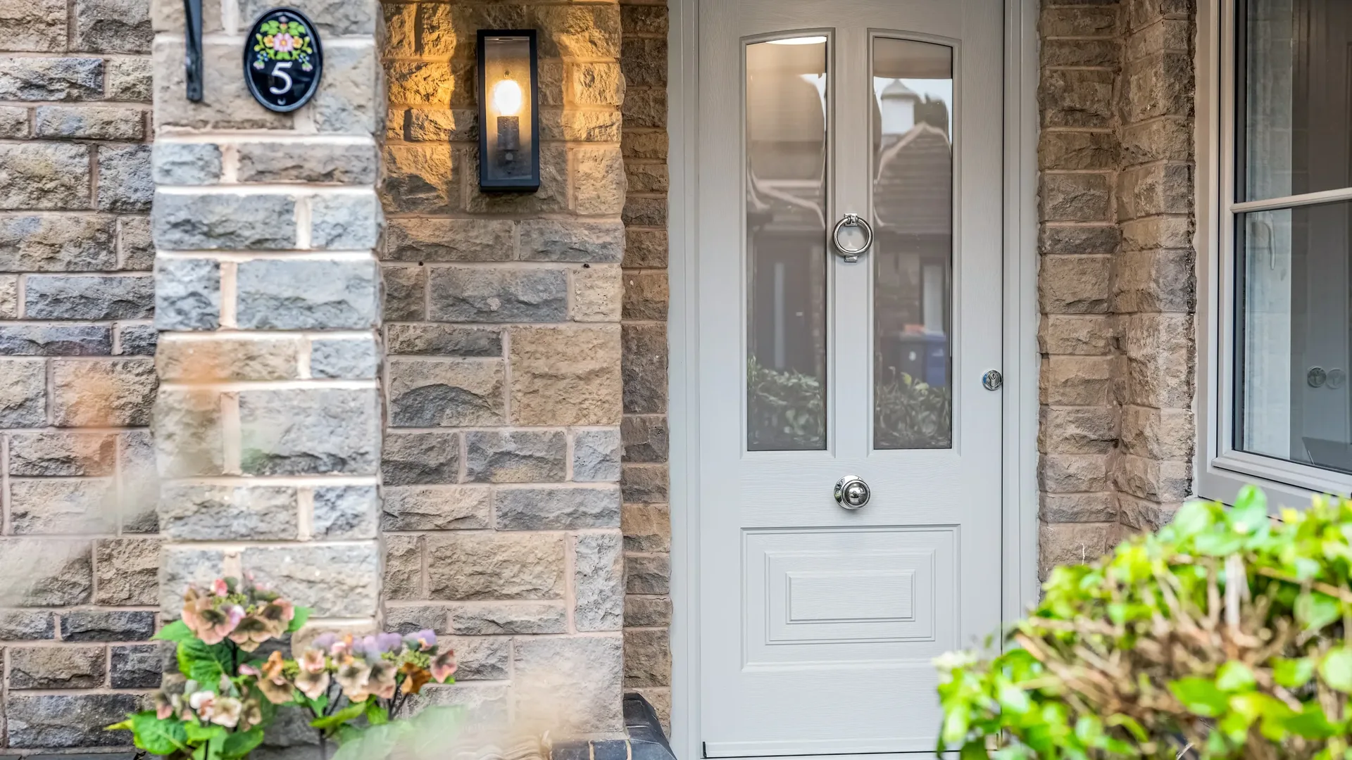 Pale grey composite front door with clear glazing and chrome ring knocker in a stone porch