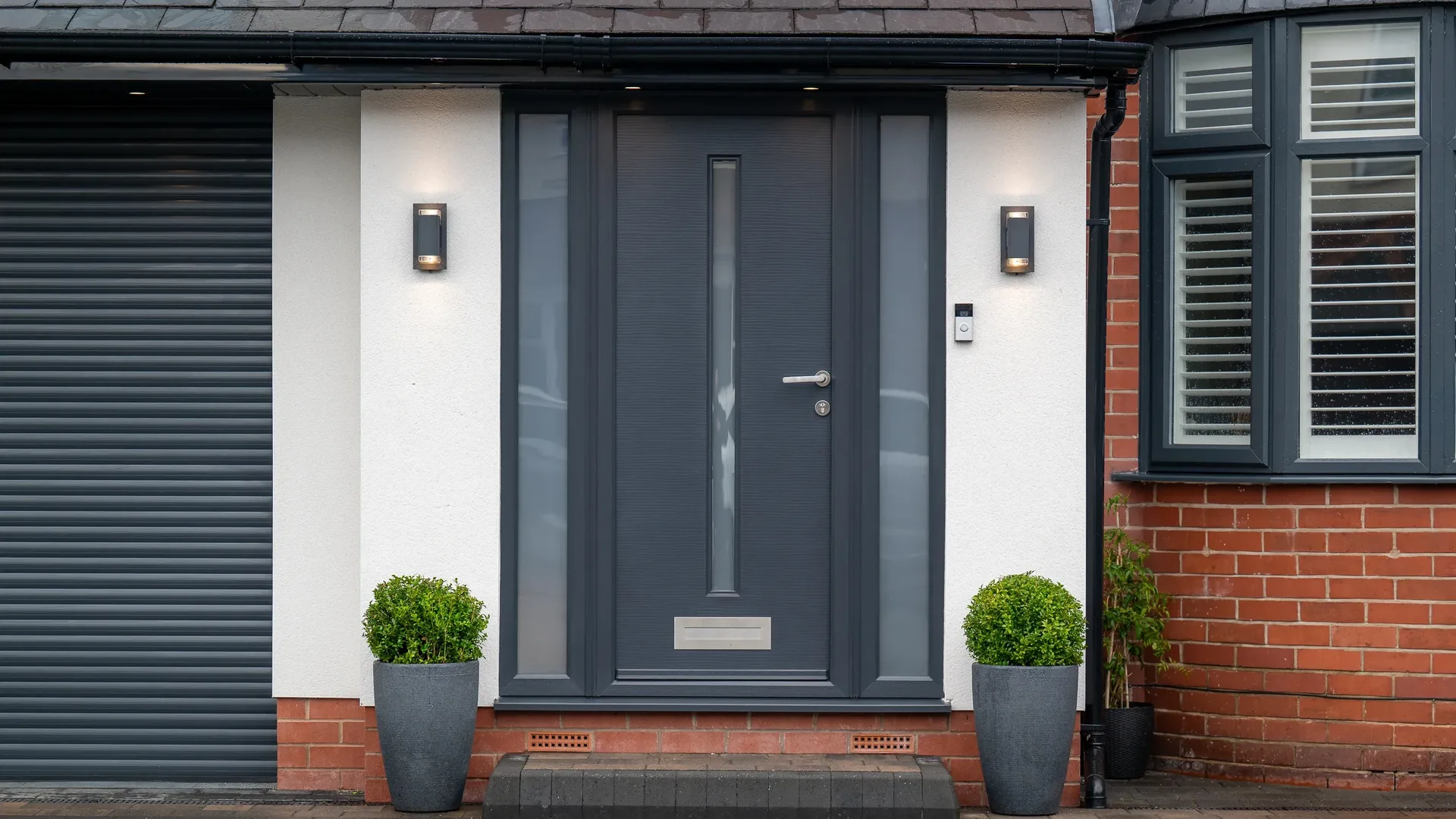 Anthracite grey composite front door with a slim glazed strip and frosted sidelights between potted shrubs