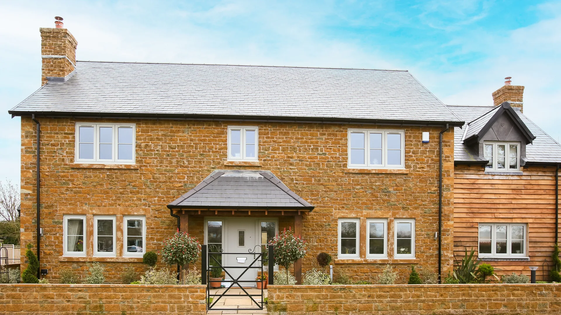 Stone detached house with pale casement windows throughout, a slate-roofed porch and a timber-clad side wing