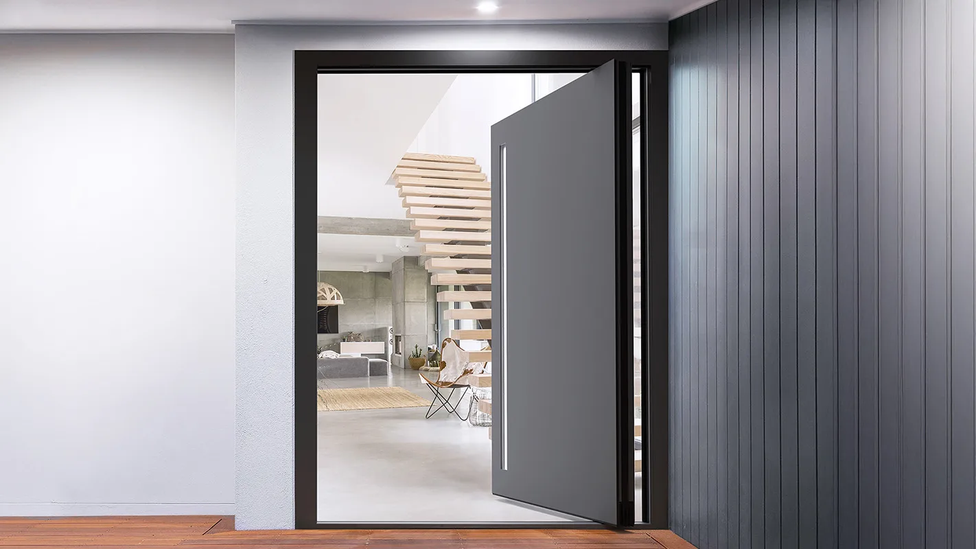 Grey aluminium pivot front door standing open onto a bright hallway with a floating timber staircase
