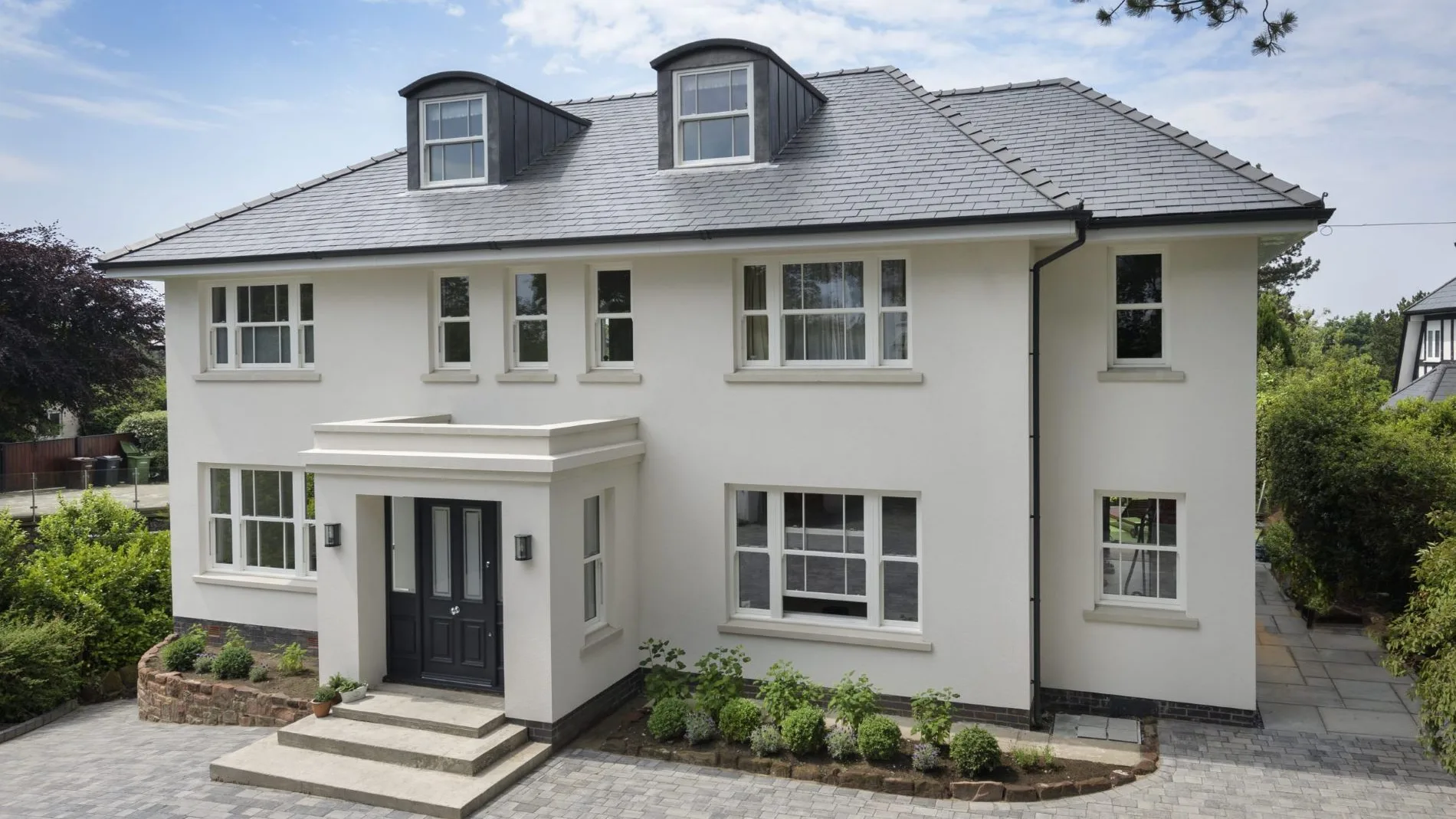 White rendered detached house with off-white sliding sash windows, dormer sashes and a black panelled front door