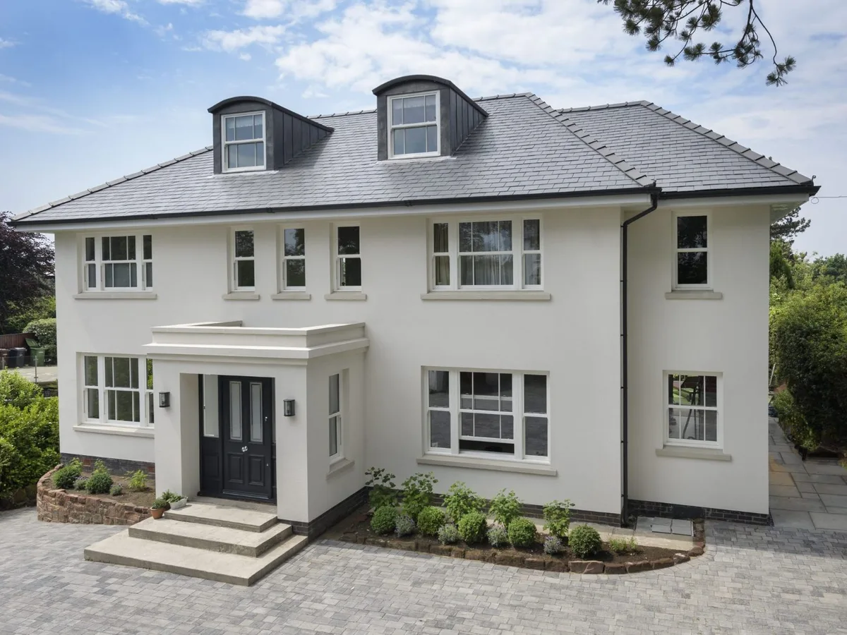 White rendered detached house with off-white sliding sash windows, dormer sashes and a black panelled front door