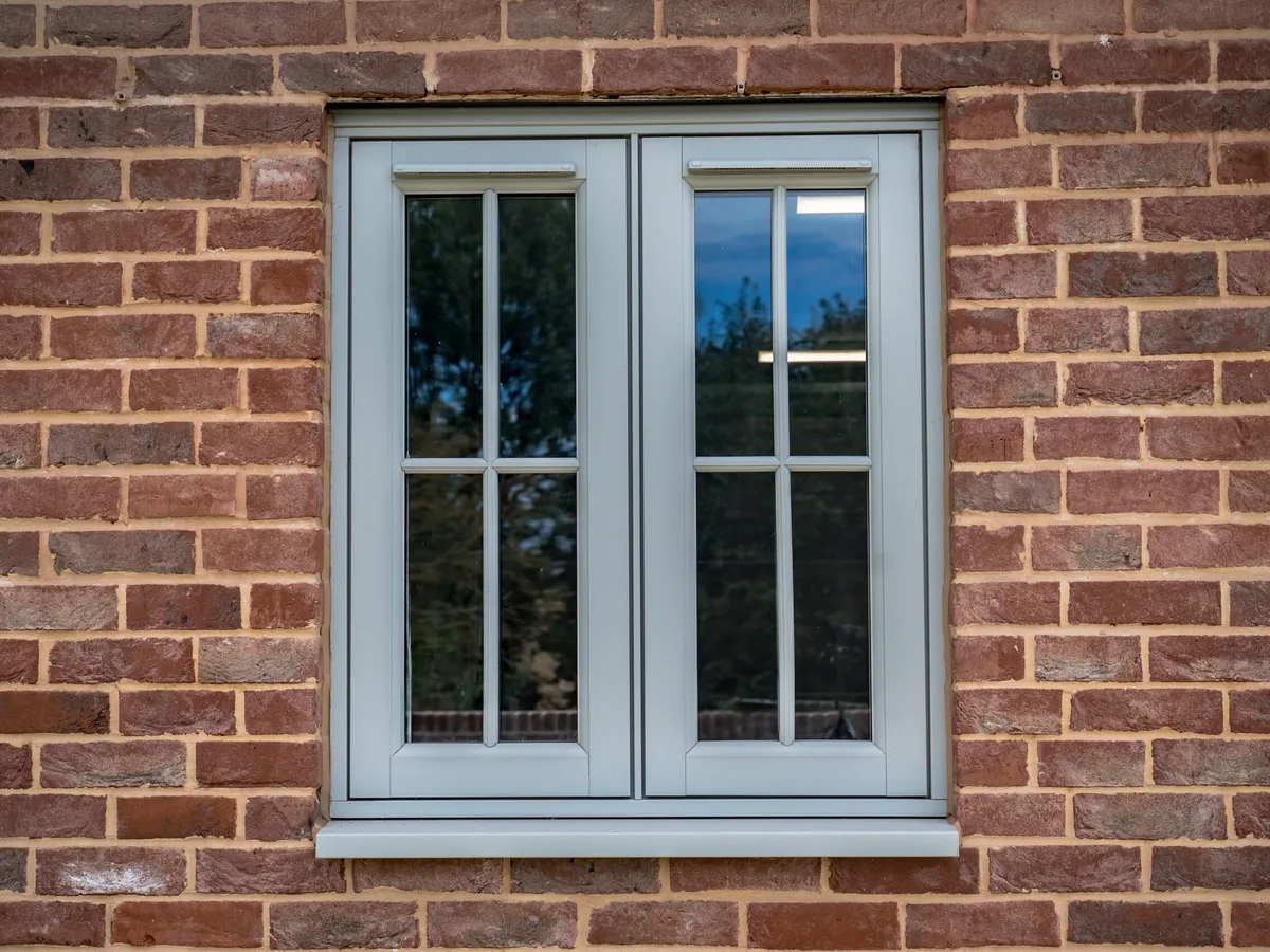 Grey-green two-pane casement window with Georgian bars set in a red brick wall
