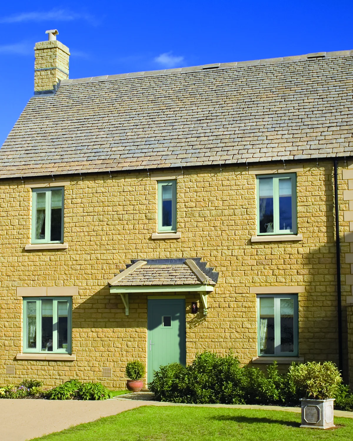 Honey-coloured stone house with pale green aluminium casement windows and a matching front door