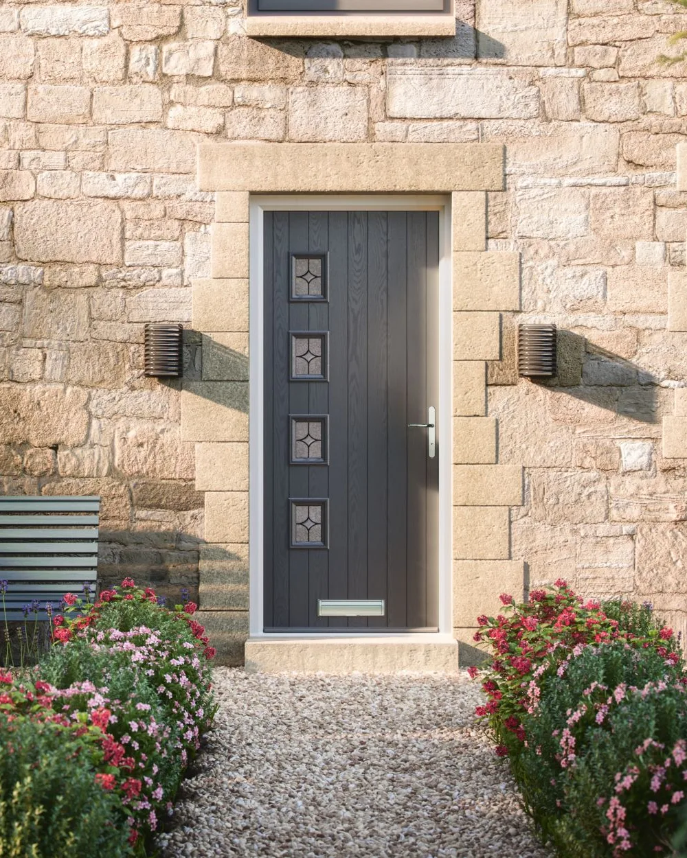 Anthracite grey composite door with four small glazed squares in a stone wall above a gravel path