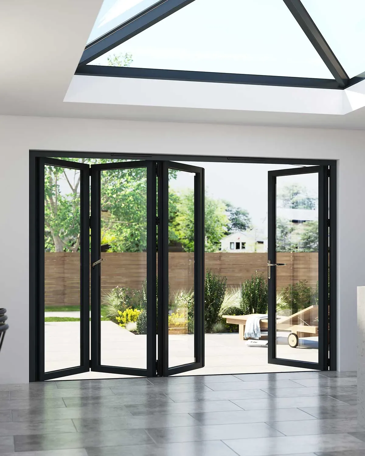 Black aluminium bifold doors folded open from a kitchen diner onto a paved garden, beneath a roof lantern