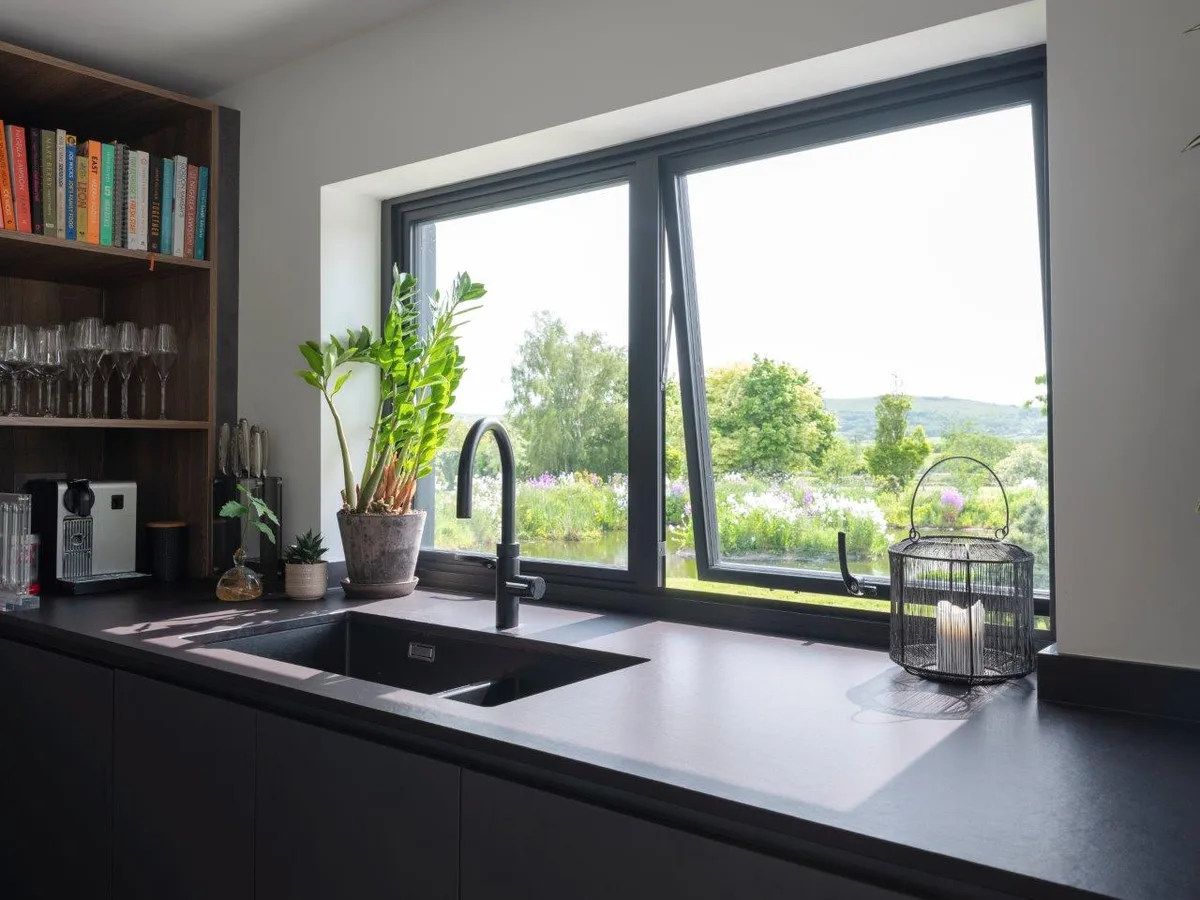 Black aluminium casement window above a kitchen sink with its top-hung vent open onto the garden