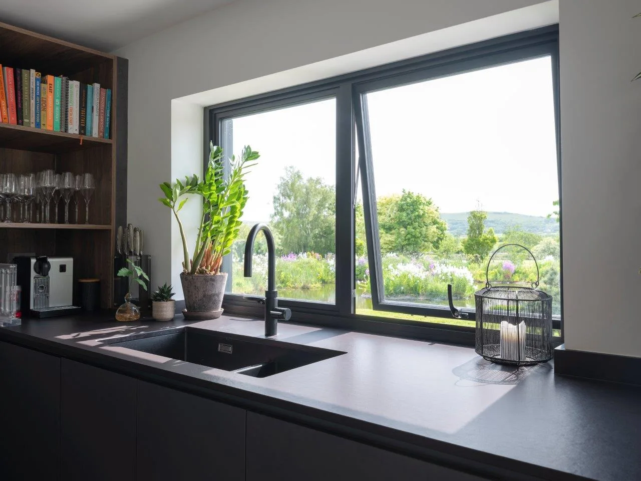 Black aluminium casement window above a kitchen sink with its top-hung vent open onto the garden