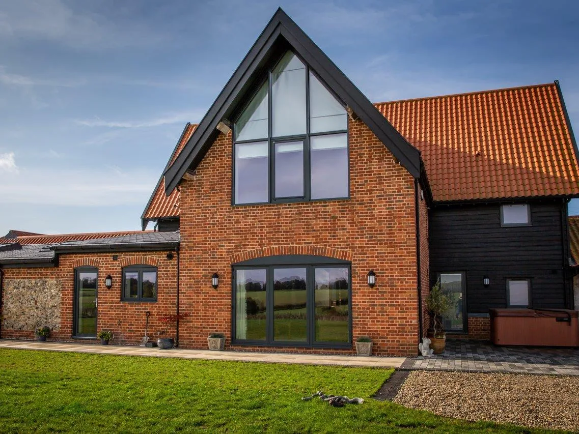 Red brick and flint home with dark grey aluminium casement windows, gable glazing and arched glazed doors