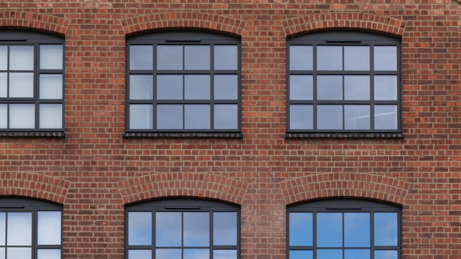 Red brick gable with dark grey aluminium heritage windows, slim glazing bars and arched brick heads
