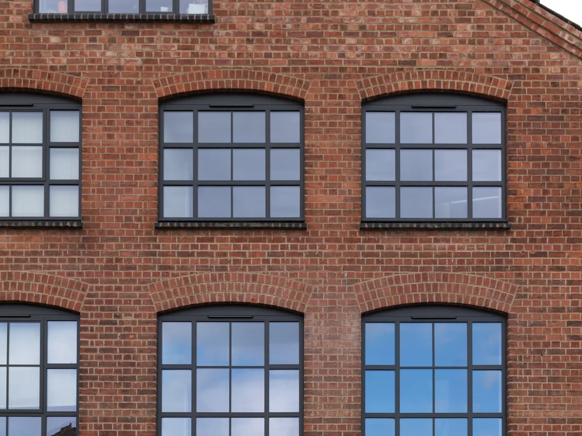 Red brick gable with dark grey aluminium heritage windows, slim glazing bars and arched brick heads