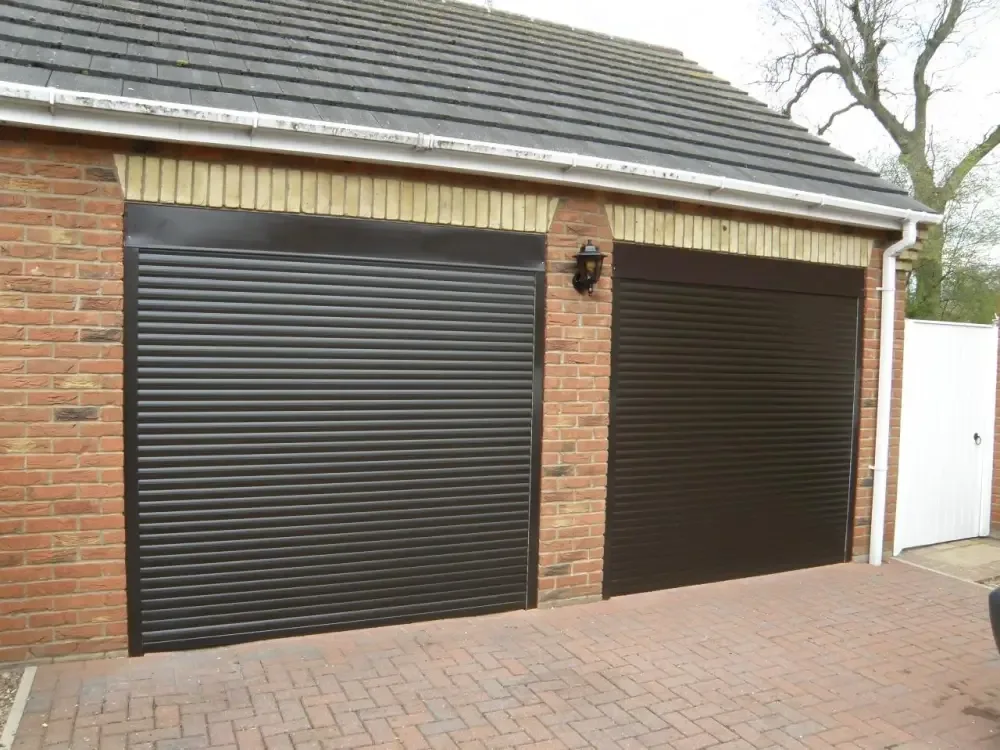 Two dark brown roller garage doors with matching boxes and guides on a red brick garage with block paving