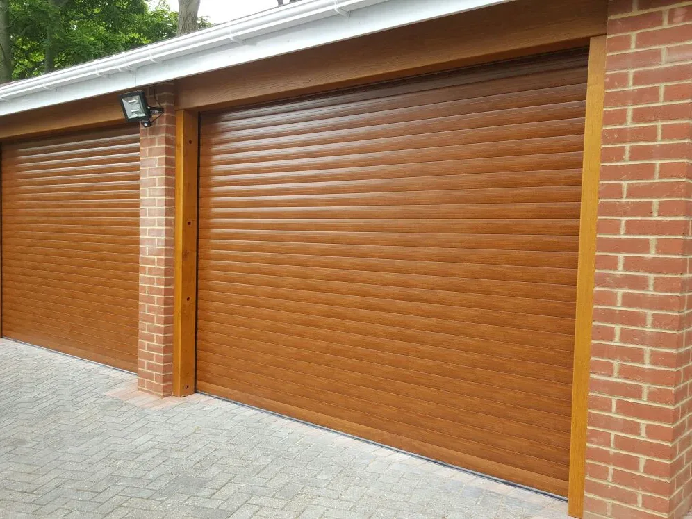 Two golden oak effect roller garage doors between red brick piers on a double garage with block paving
