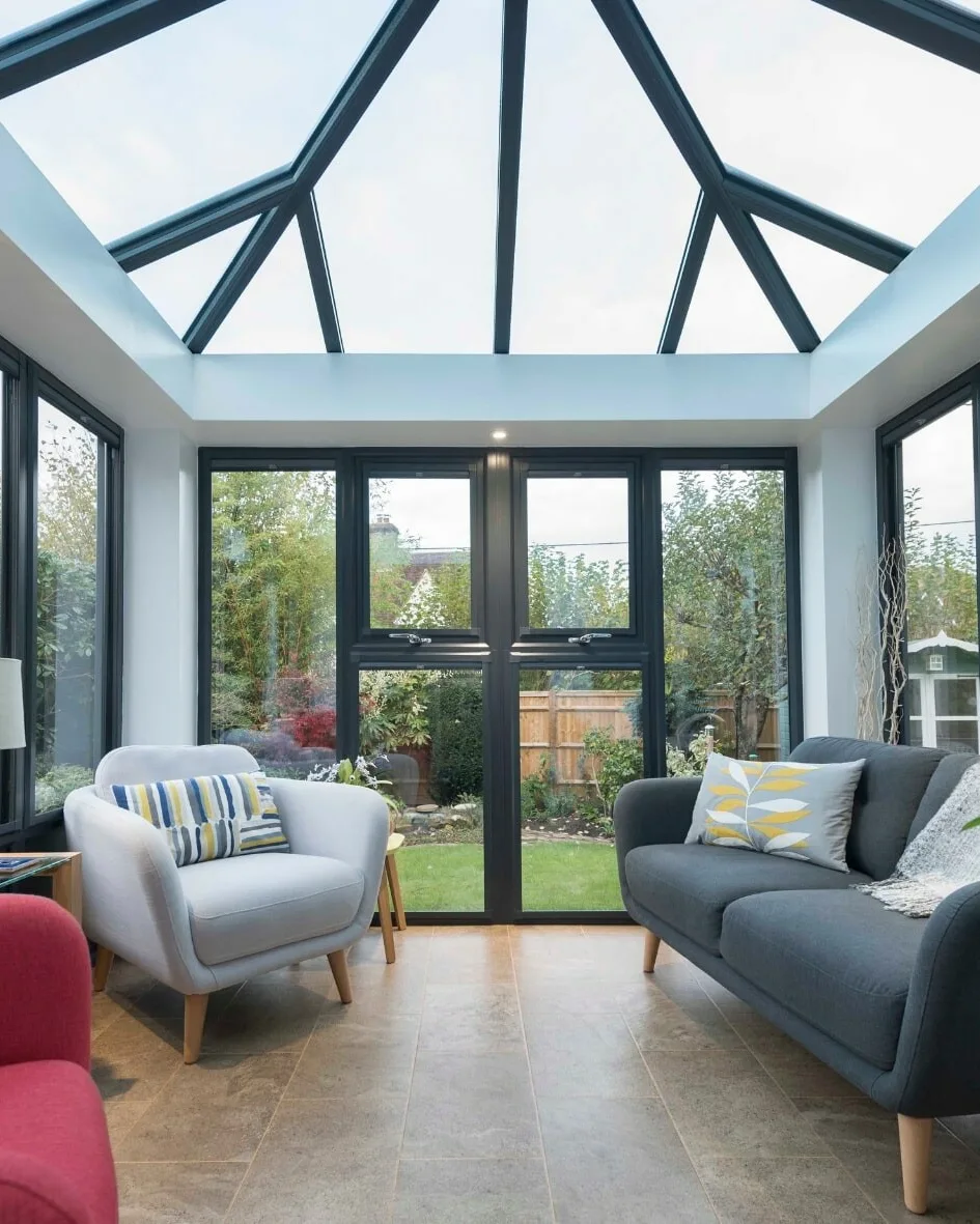 Conservatory interior with a glazed roof and grey frames, armchair and sofa, and French doors onto the garden