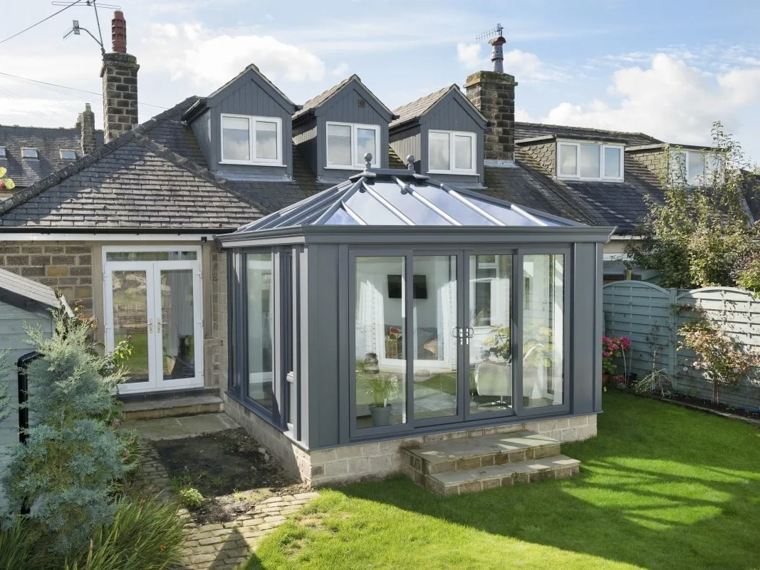 Grey-framed conservatory with a glazed roof and French doors on a stone house with dormer windows