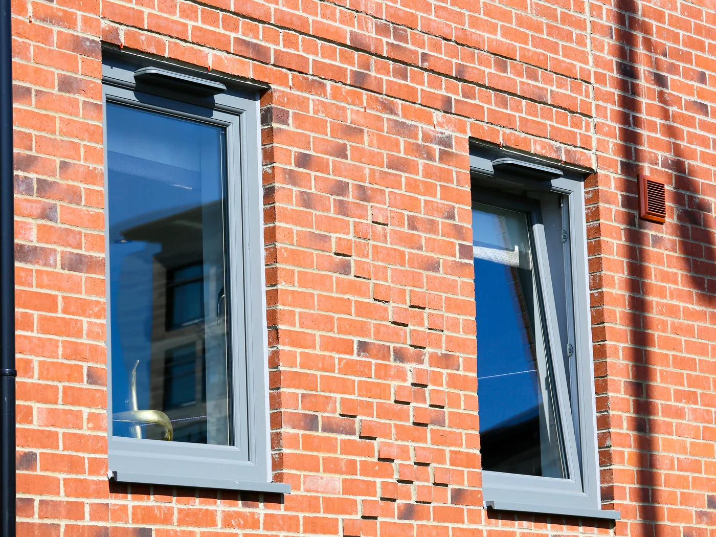 Two grey tilt and turn windows in a red brick wall, the right-hand sash tilted inward at the top