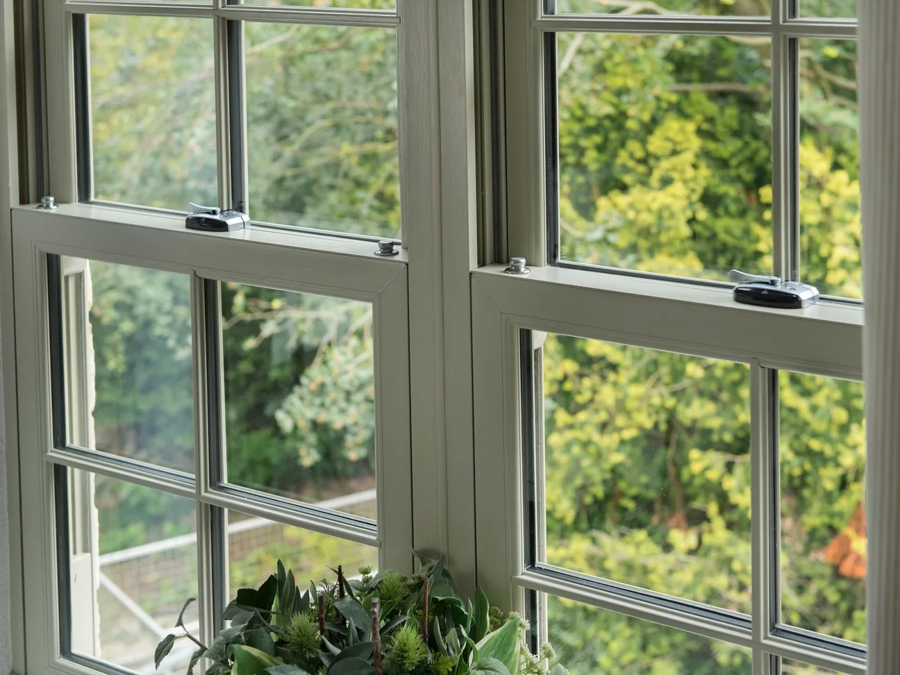 Cream woodgrain sliding sash windows with chrome locking catches, seen from inside looking out to trees