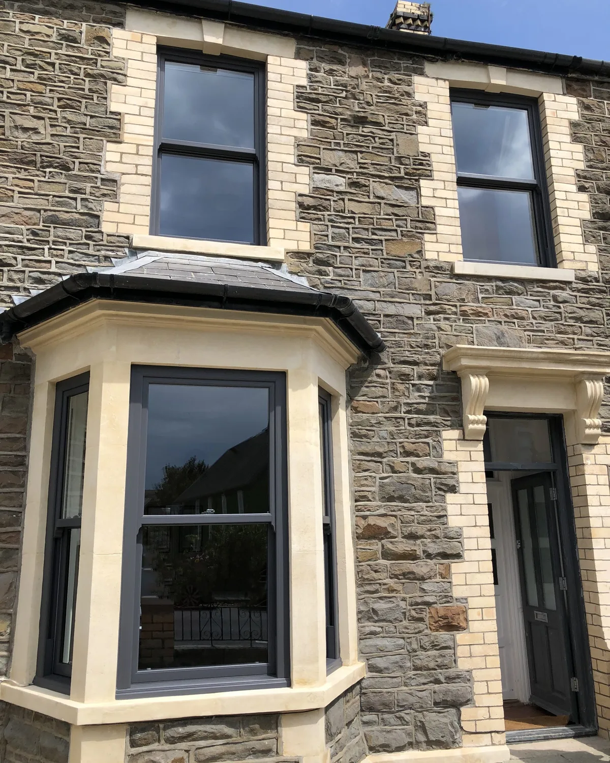 Dark grey sliding sash windows in the bay and upper floor of a stone Victorian terraced house
