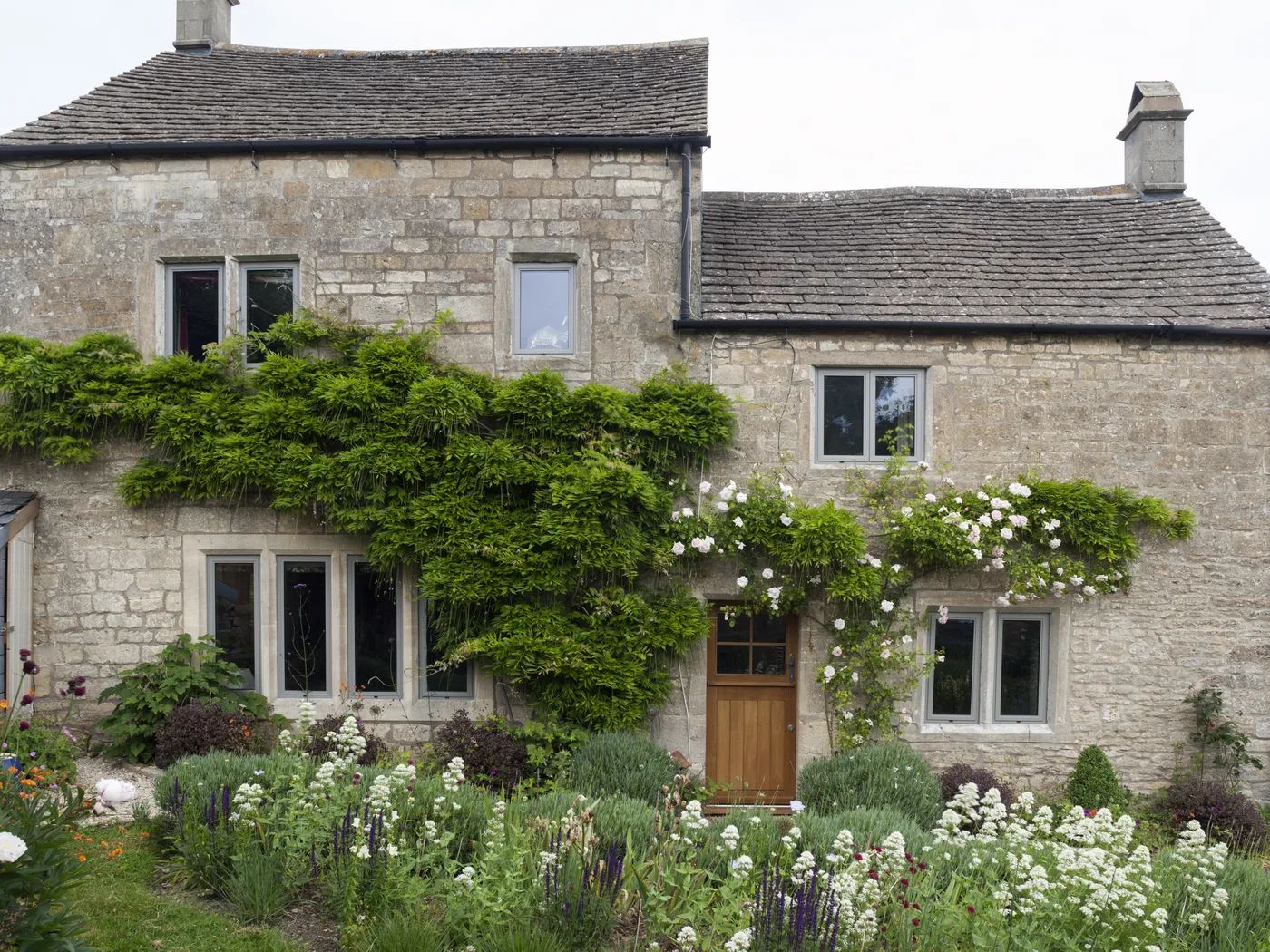 Stone cottage with light grey aluminium heritage casement windows, wisteria and a cottage garden