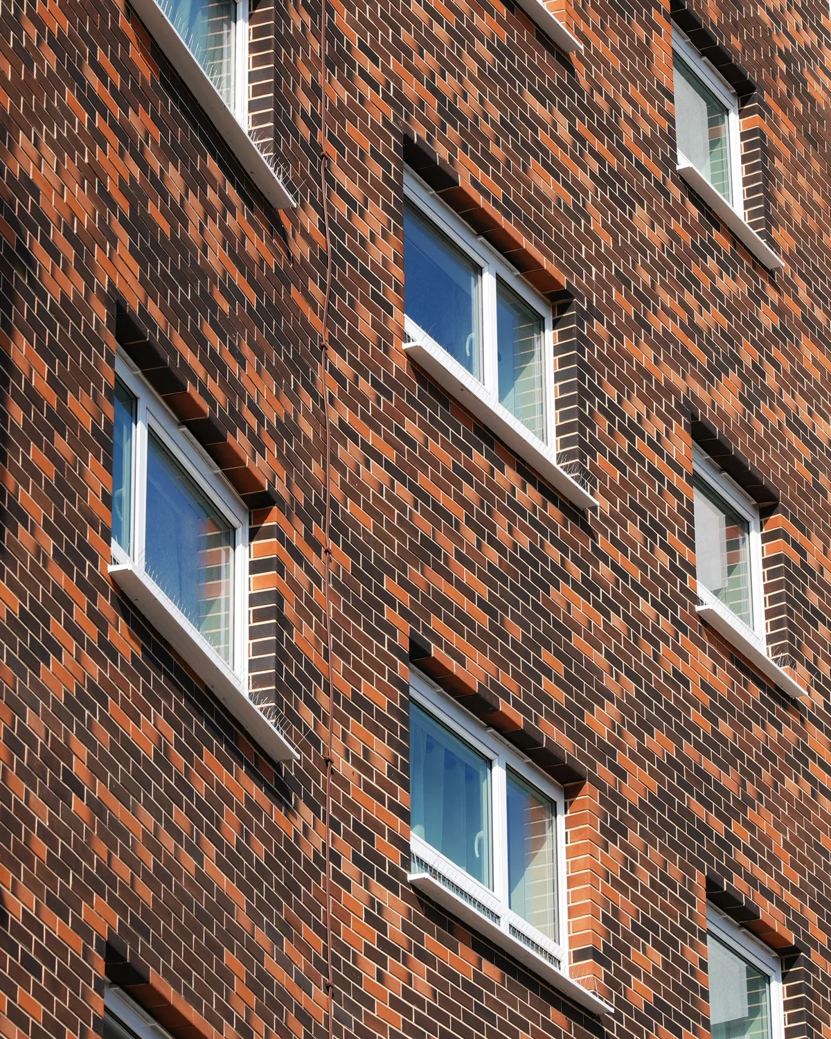 White aluminium tilt and turn windows set in the patterned brick facade of a residential tower block