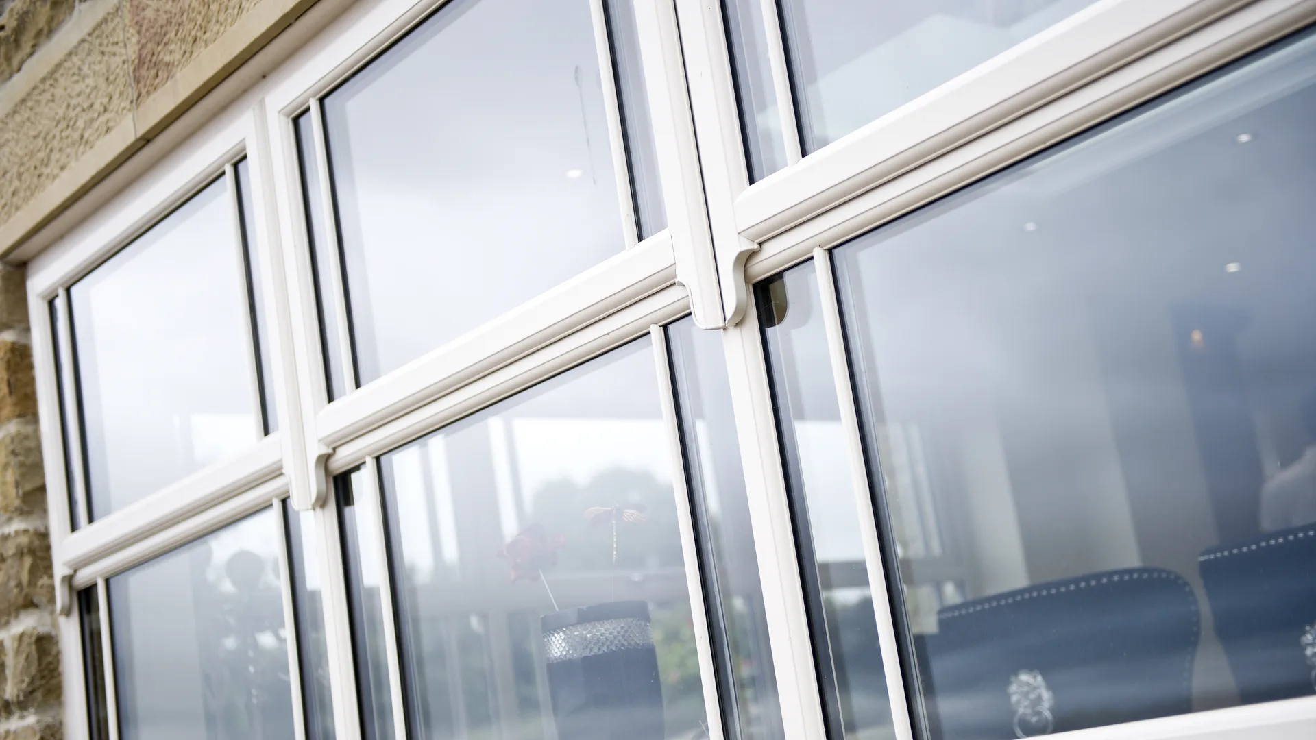 White casement windows with decorative sash horns and glazing bars set in a sandstone wall